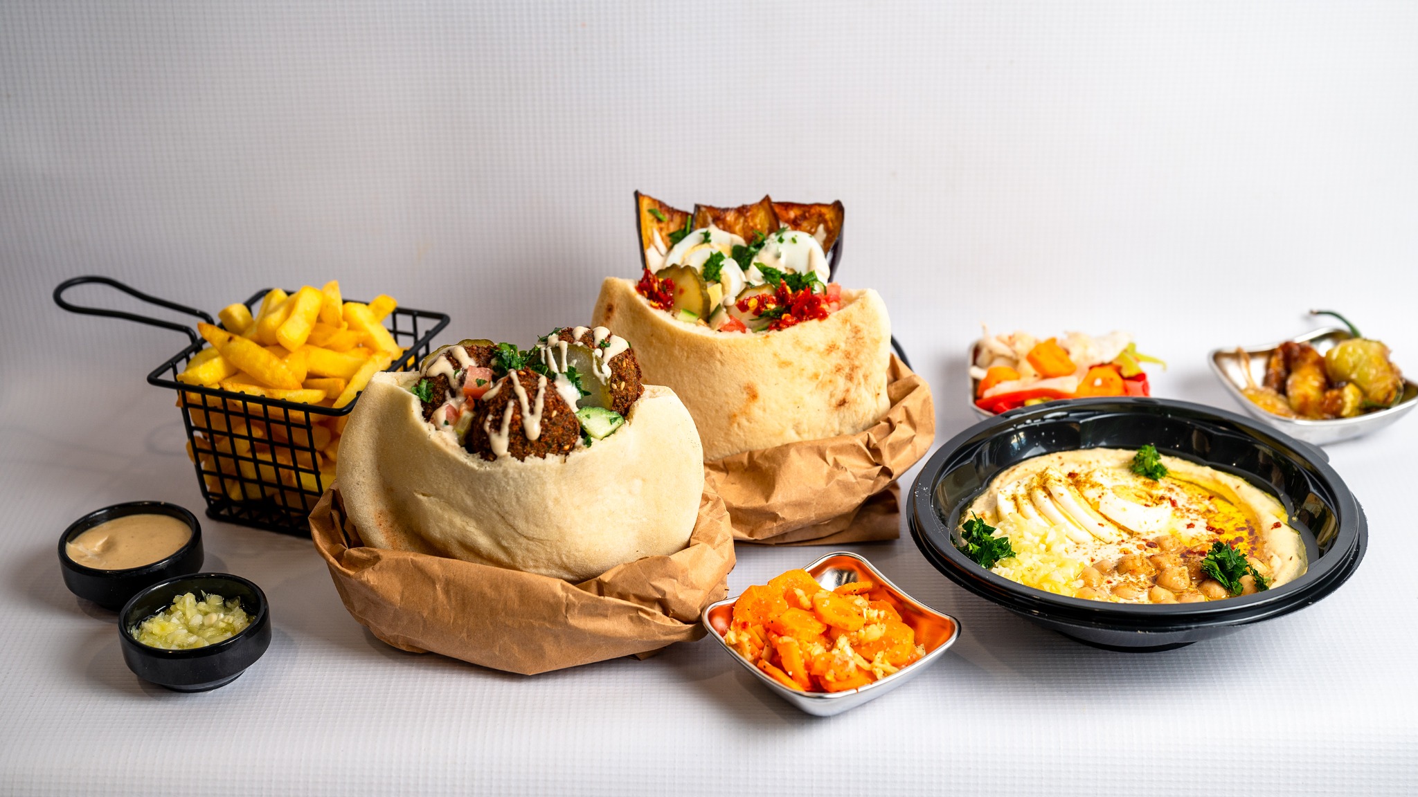 Falafel and sabich pitas, hummus, fries and salads on the table